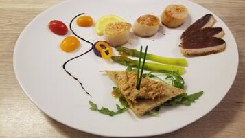 Un plato blanco con diversos alimentos, como vieiras, carne y verduras.