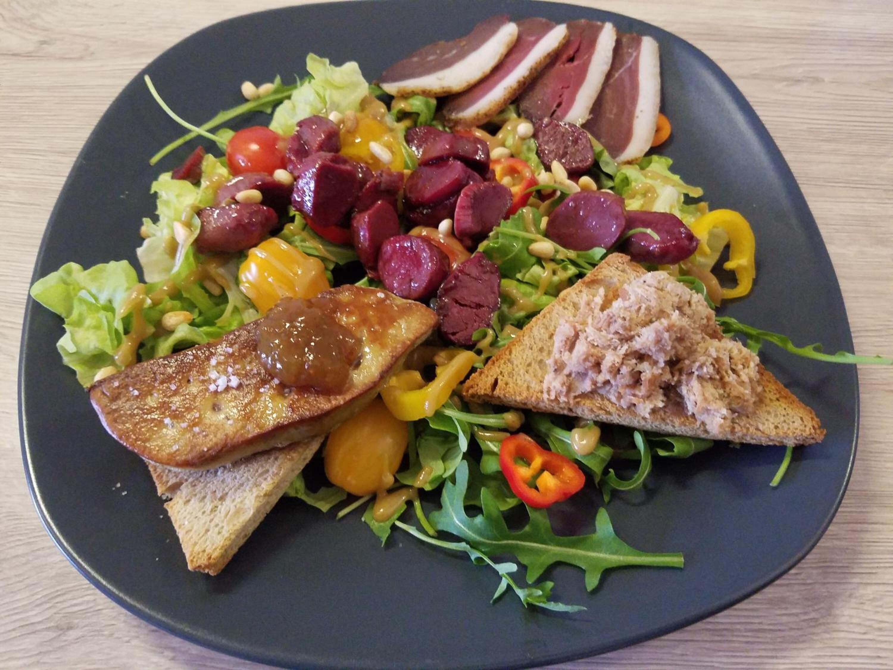 A plate with a salad, slices of meat, and two pieces of toasted bread.