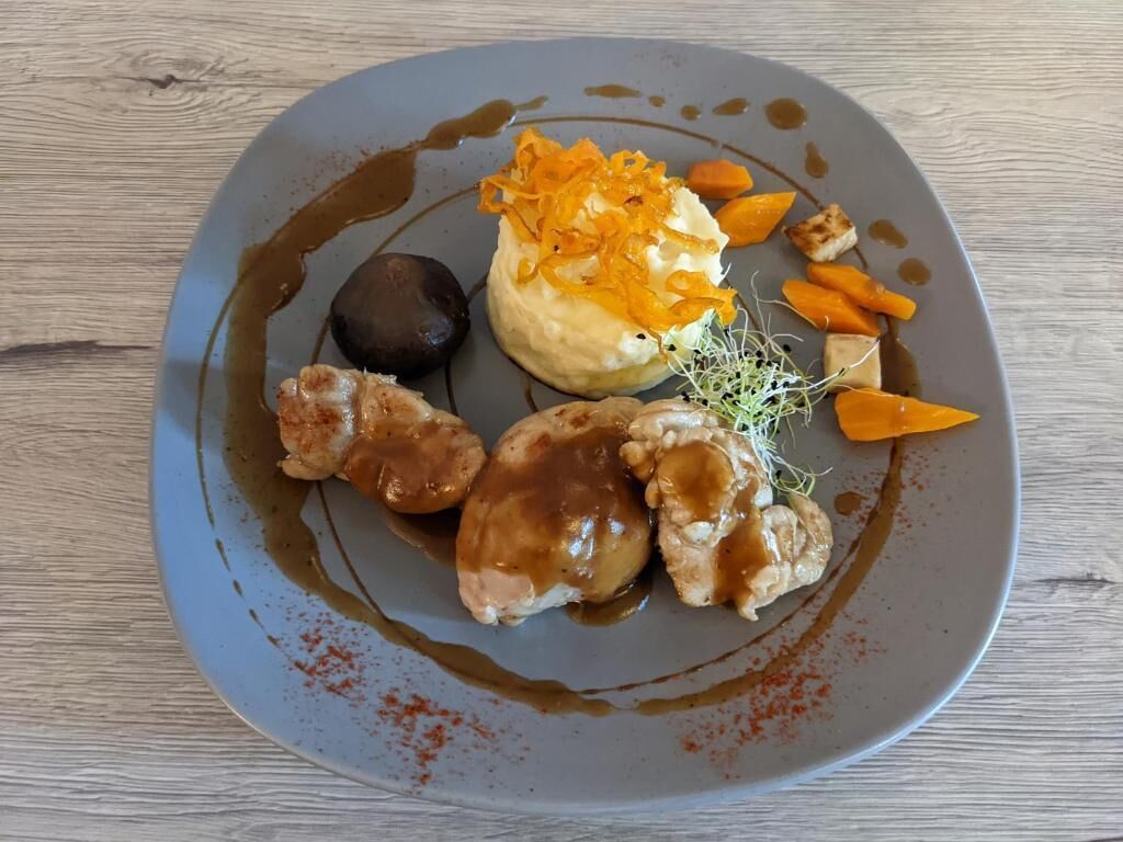 Un piatto con vari alimenti, tra cui purè di patate guarnito con scorza d'arancia, una sfera scura e un pezzo di carne con salsa.