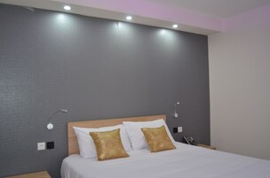 Quarto de hotel com cama grande, duas mesas de cabeceira, um criado-mudo e uma luminária fixada na parede.
