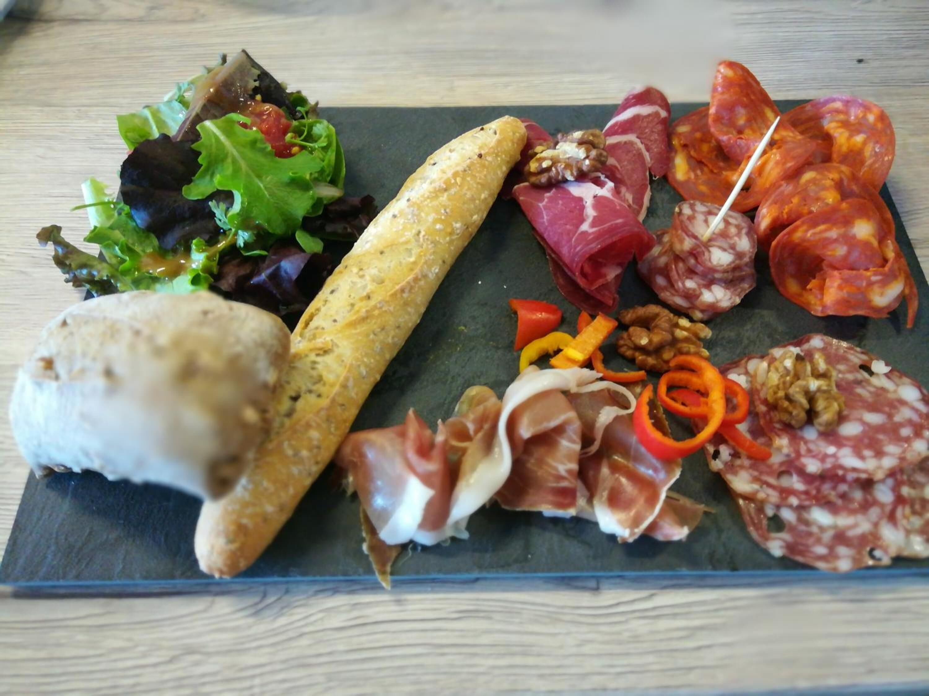 A charcuterie board with various meats, nuts, and a baguette on a slate plate.