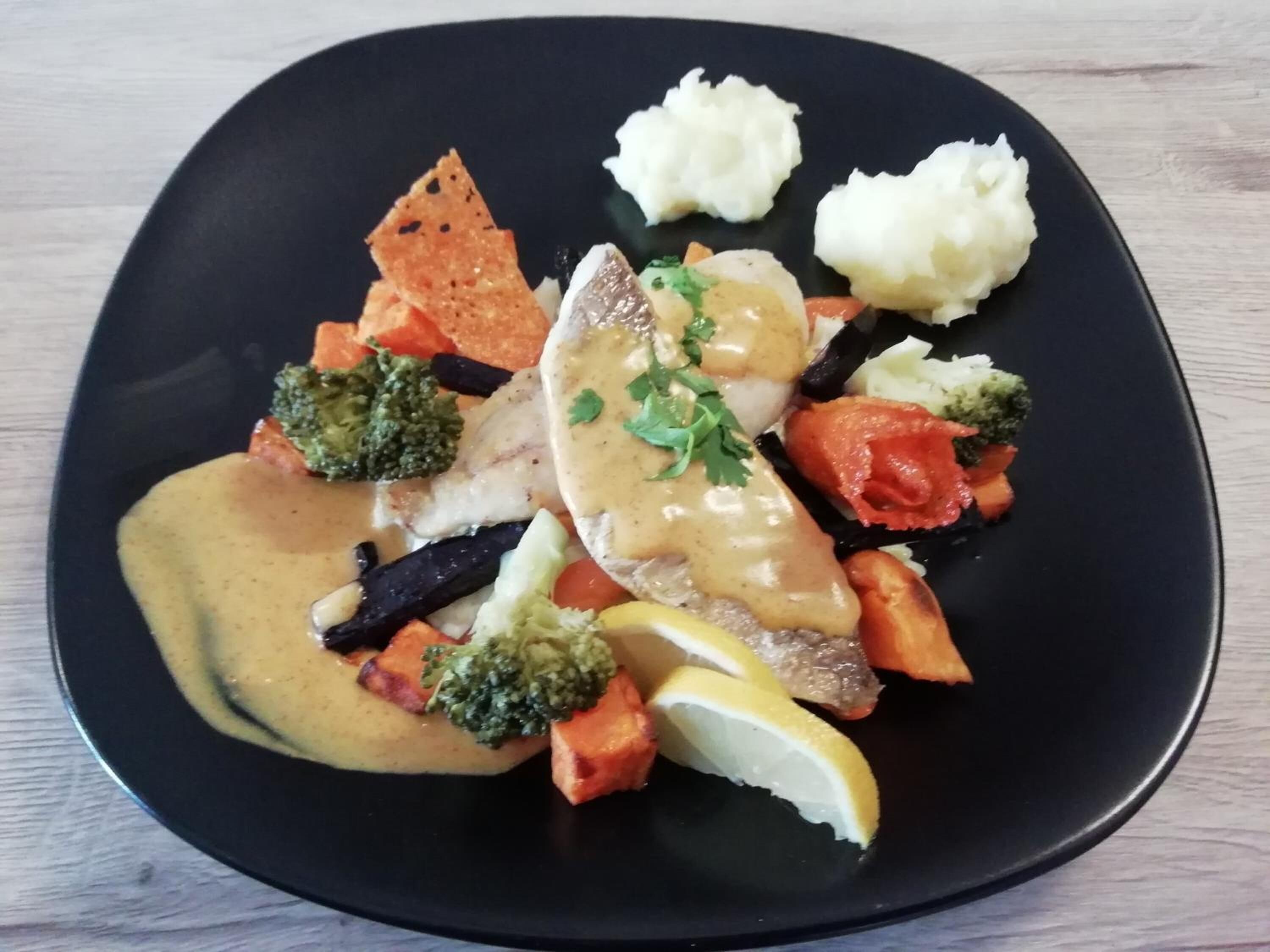Un plato rectangular con diversos alimentos, incluyendo pescado, verduras y puré de papas.