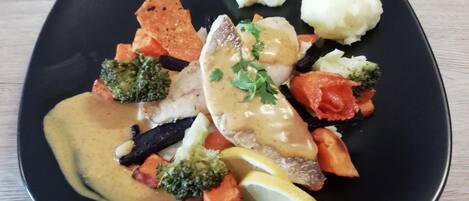 Un plato rectangular con diversos alimentos, incluyendo pescado, verduras y puré de papas.