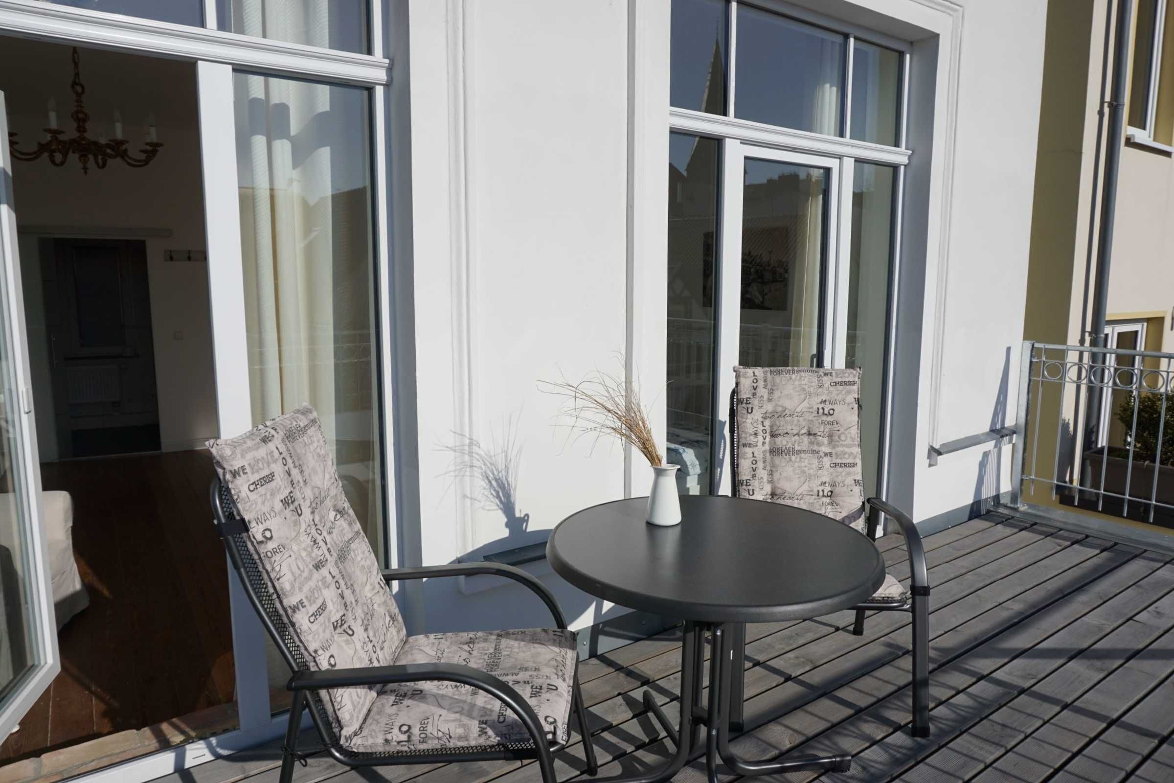 A balcony with a round table and two chairs, large windows, and a visible door.