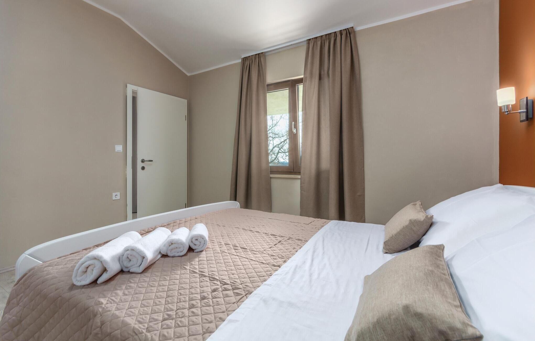 A hotel room with a bed, a window with curtains, a door, and a wall-mounted light.