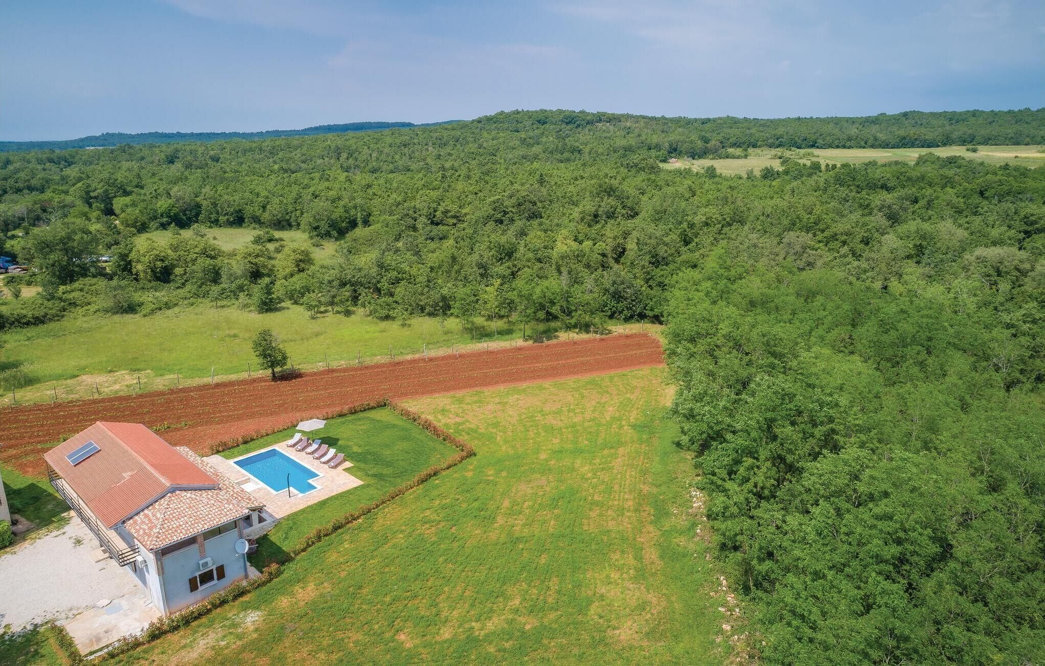 Una casa con piscina, rodeada de campos verdes y árboles.