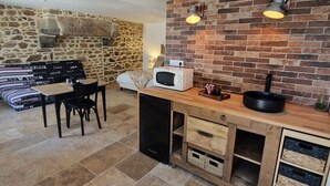 A kitchen with a stone wall, a wooden countertop, and a dining area with a table and chairs. - Au fer à cheval (Gandelain)