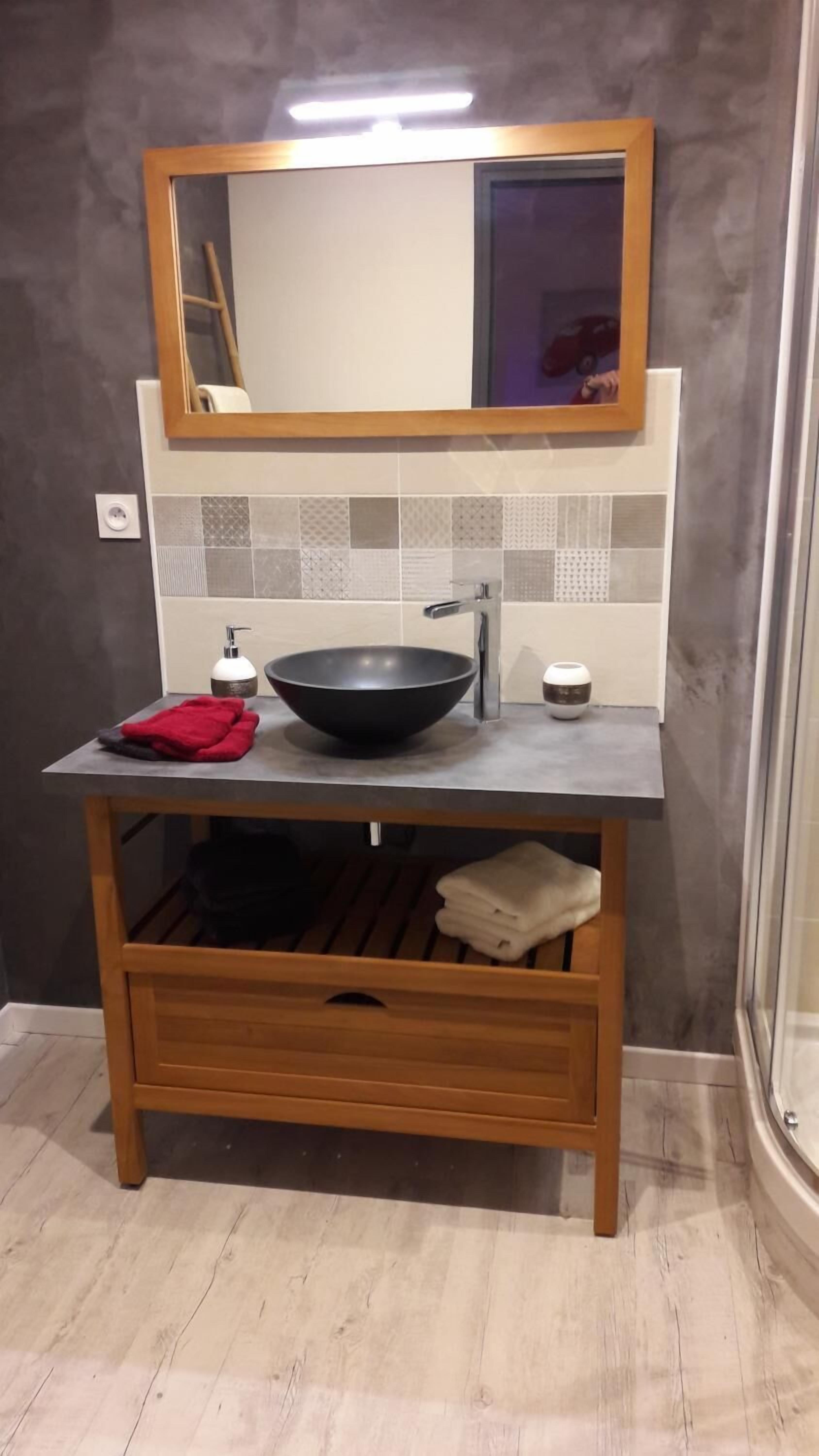 A bathroom with a wooden vanity, a black basin, a mirror, and a towel rack.
