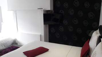 A hotel room with a white bed, a red pillow, a black wall with a circular pattern, and a mounted TV.