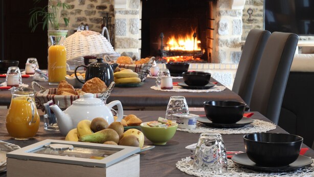 A breakfast table set with various breakfast items, a fireplace, and stone walls. - Au fer à cheval (Gandelain)
