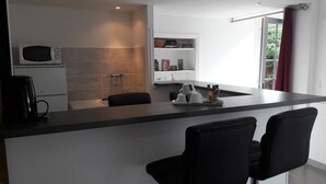 A modern kitchen with a black countertop, a microwave, a coffee maker, and a shelf with books and kitchen items. - Au fer à cheval (Gandelain)