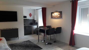 Un espacio habitable compacto con comedor, kitchenette y televisor montado en la pared.