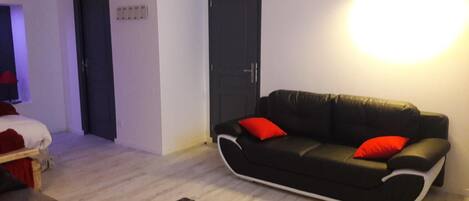 Un salón moderno con un sofá negro, cojines rojos, una mesa de madera y una lámpara.