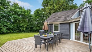 Une terrasse avec une table et des chaises, un barbecue couvert et une porte-fenêtre coulissante donnant sur un patio.