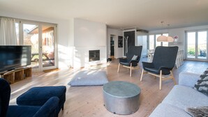 Una sala de estar moderna con televisor, asientos cómodos, chimenea y ventanas grandes.