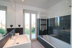 Un baño moderno con una bañera grande, zona de ducha separada y tocador con lavabo.