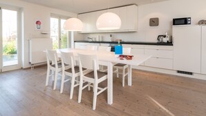 Una cocina moderna con muebles blancos, una mesa de comedor con cuatro sillas y un microondas en la encimera.
