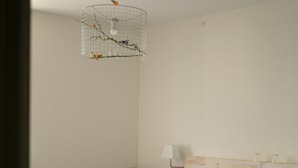 A bedroom with a wooden headboard, a bed with blue bedding, a nightstand with a lamp, and a birdcage with a hanging light fixture.
