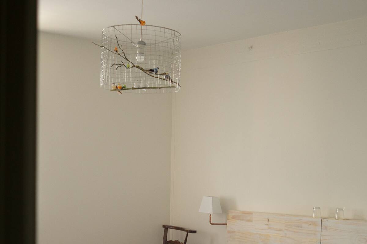 A bedroom with a wooden headboard, a bed with blue bedding, a nightstand with a lamp, and a birdcage with a hanging light fixture.