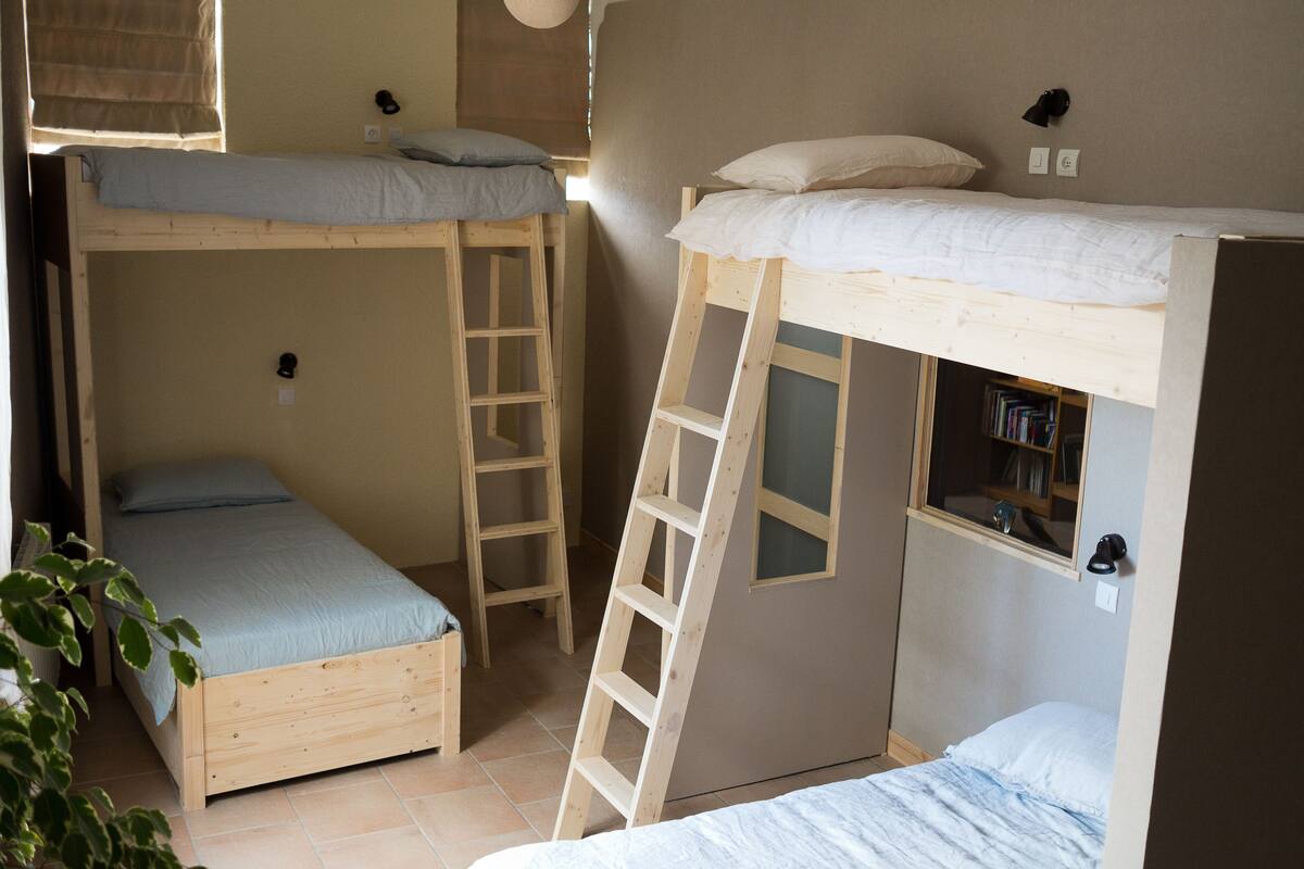 A dormitory-style room with bunk beds, a ladder, and a bookshelf.