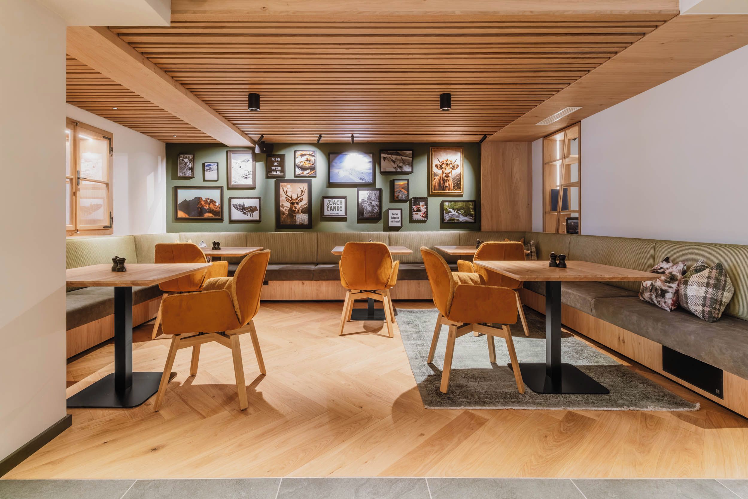 Un interior moderno con vigas de madera en el techo, una zona de estar con mesas y sillas, y una pared decorada con cuadros enmarcados.
