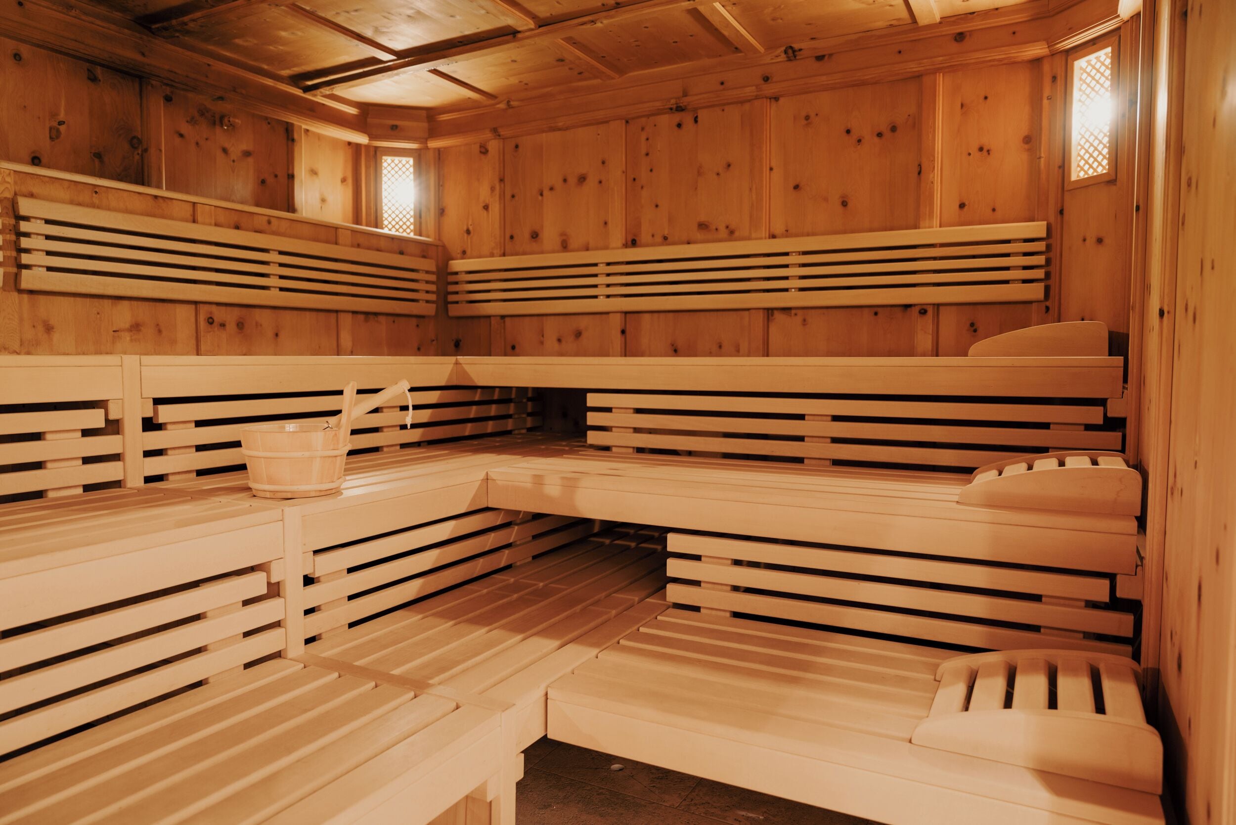 A sauna with wooden benches and benches, a bucket, and a wooden wall with a lattice window.
