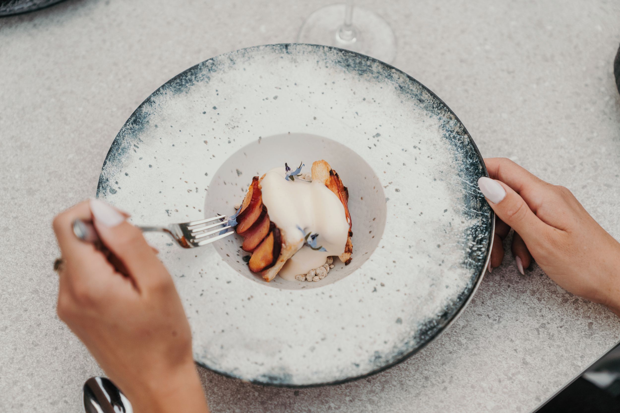 A person holding a plate with a dessert, using a fork.