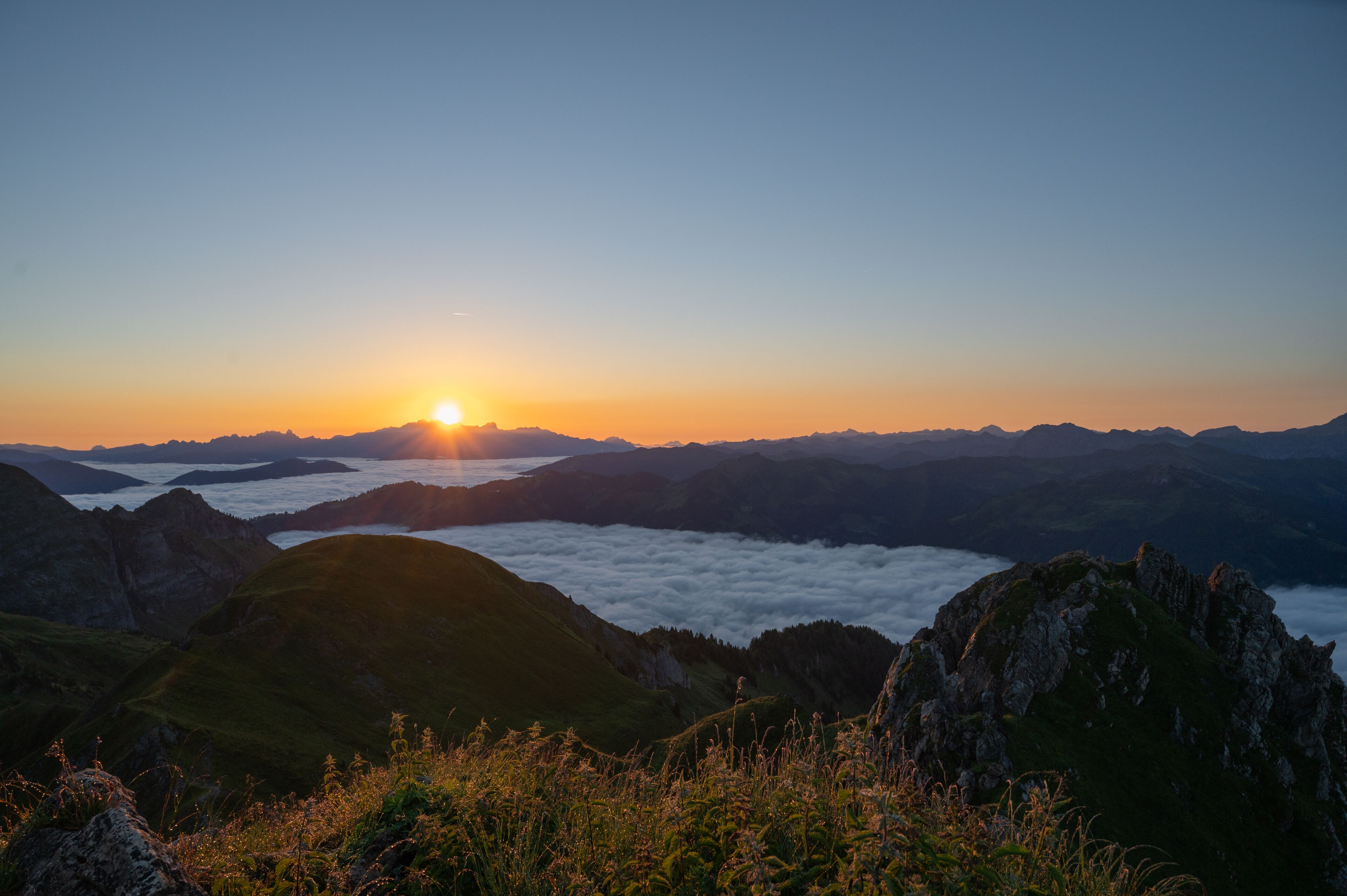 A mountain landscape with a sunrise, featuring rolling hills and a valley below.