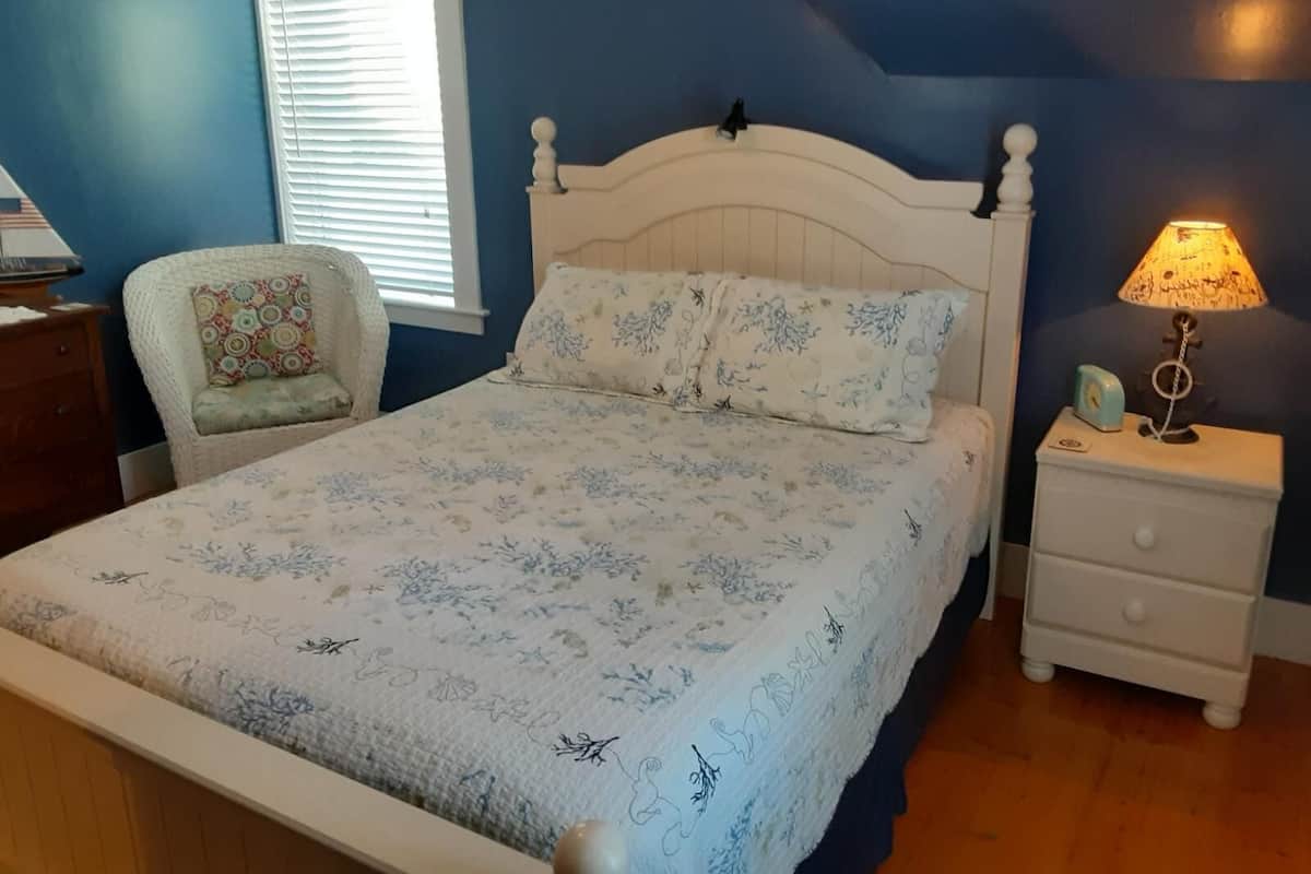 A bedroom with a bed, a nightstand, a chair, and a window with blinds.