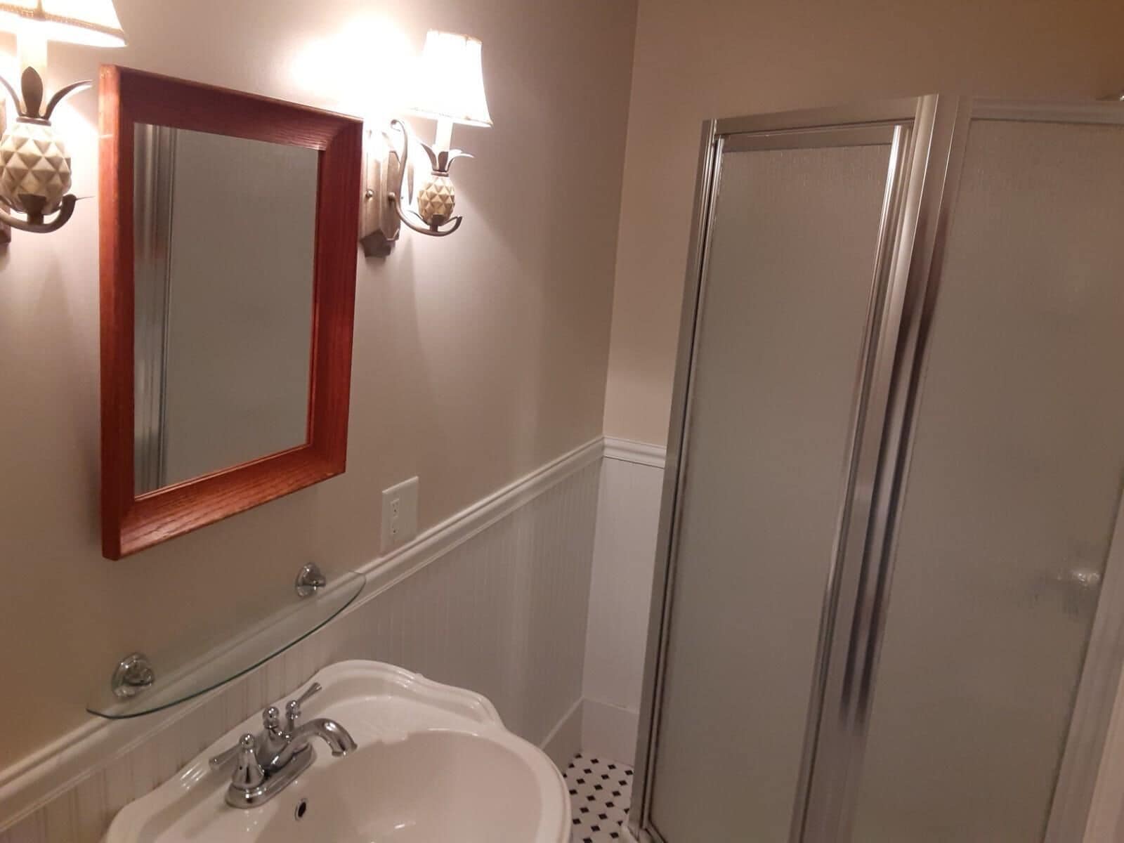 A bathroom with a white sink, a mirror with a wooden frame, and a shower area.