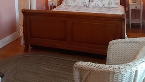 A bedroom with a wooden bed, two bedside lamps, a chandelier, and a wicker chair. - Bittersweet Bed and Breakfast (York Beach)