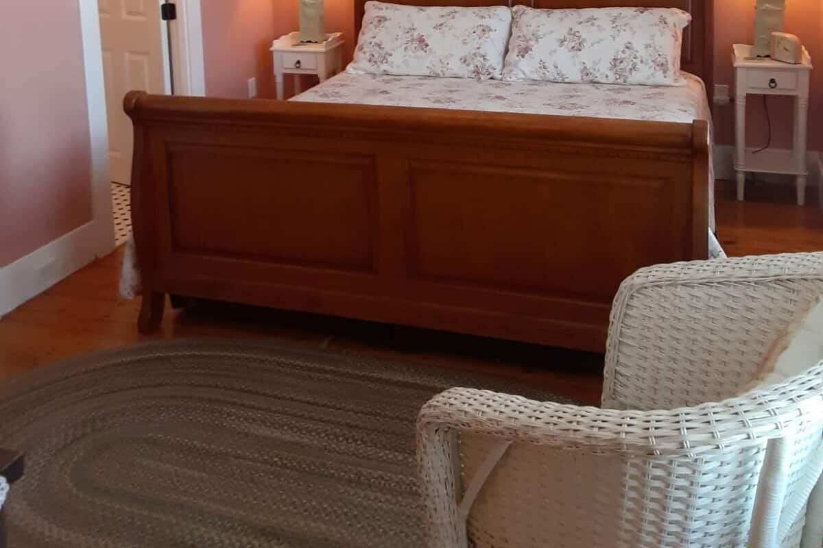 A bedroom with a wooden bed, two bedside lamps, a chandelier, and a wicker chair.