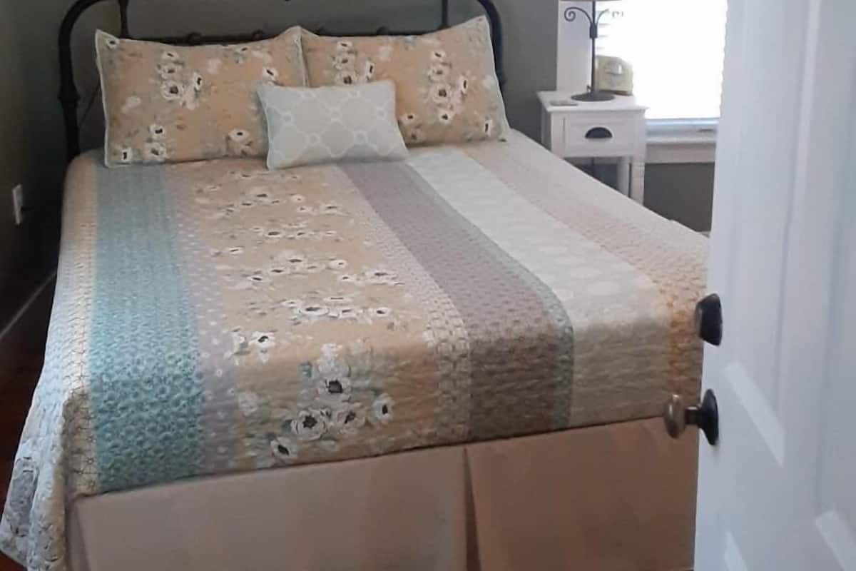 A bedroom with a bed, a nightstand, a lamp, and a window.