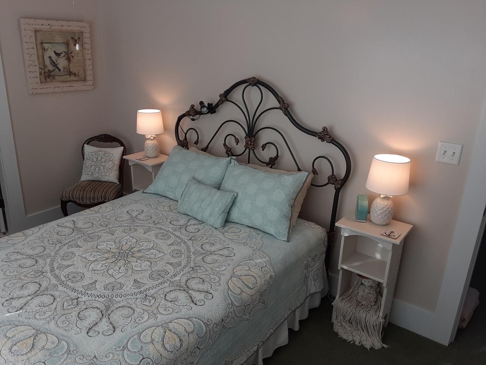 A neatly arranged bedroom with a bed, two bedside tables, a chair, and a wall-mounted picture.