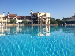 Ein großer Swimmingpool mit klarem, blauem Wasser, umgeben von Gebäuden mit Balkonen und einem wolkenlosen Himmel.