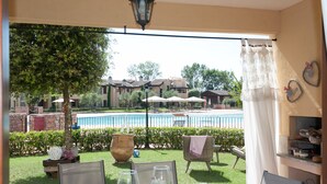 A patio with a table set for dining, a pool, and a view of a residential area. - Lugana Village Resort & Sporting Club (Peschiera del Garda)