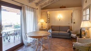 A cozy living room with a round table, a sofa, and a wicker chair. There is a balcony with a table and chairs outside. - Lugana Village Resort & Sporting Club (Peschiera del Garda)