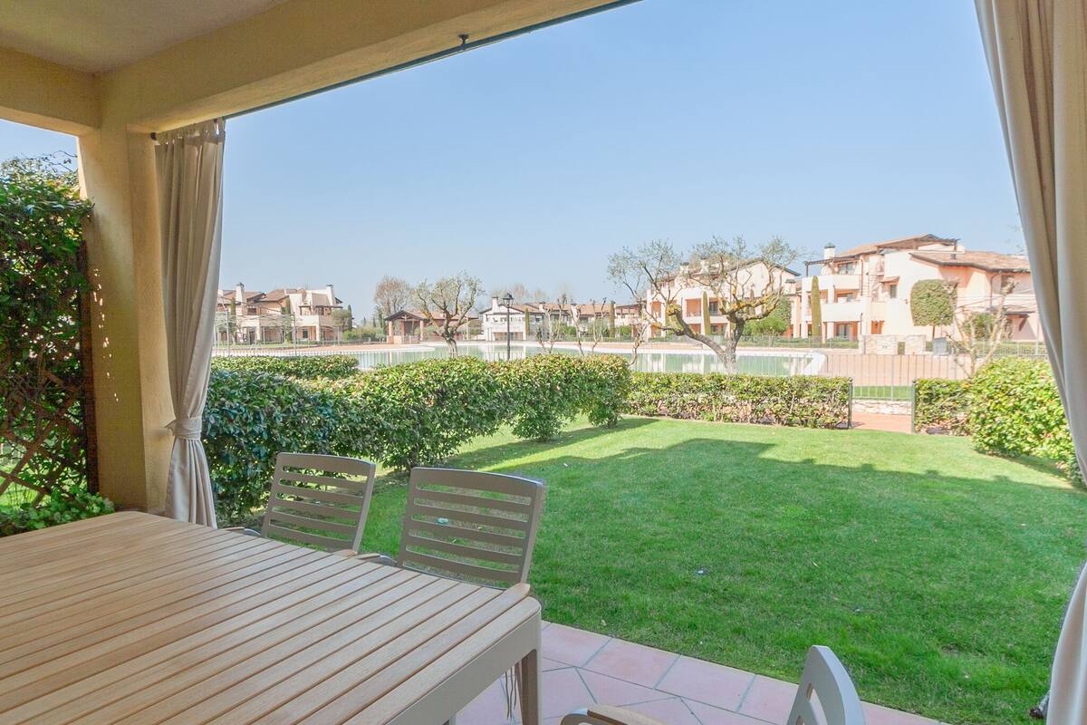 Une terrasse avec une table et des chaises, une vue sur une pelouse bien entretenue et, au loin, une rangée de maisons.