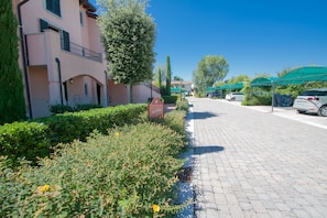 A paved driveway leading to a building with a balcony, surrounded by greenery and parked cars. - Lugana Village Resort & Sporting Club (Peschiera del Garda)