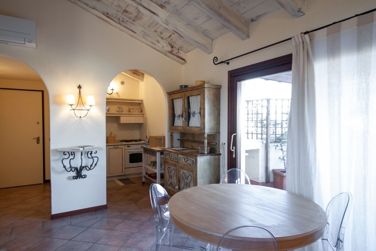 Une cuisine compacte avec un coin repas, comprenant une table et des chaises en bois rondes, un four encastré et une fenêtre avec des rideaux.