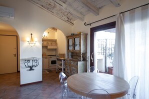 Une cuisine compacte avec un coin repas, comprenant une table et des chaises en bois rondes, un four encastré et une fenêtre avec des rideaux.