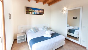 A hotel room with a bed, a nightstand, a mirror, and a painting on the wall. - Lugana Village Resort & Sporting Club (Peschiera del Garda)