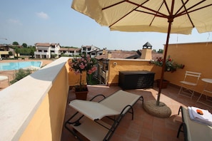 A rooftop terrace with a pool, lounge chairs, an umbrella, and potted plants. - Lugana Village Resort & Sporting Club (Peschiera del Garda)