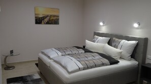 Une chambre à coucher moderne avec un grand lit, une table de chevet, une petite table ronde et un tableau au mur.