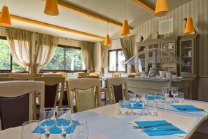 Un comedor con mesas dispuestas para comer, sillas e iluminación colgante.