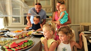 Une famille est assise à table, devant une variété de plats, et un buffet est installé à proximité.