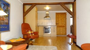 A spacious living room with a wooden ceiling, a kitchen with a stove and cabinets, and a wooden door.