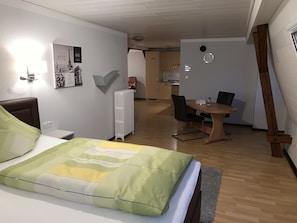 Una camera d'albergo con un letto, una scrivania, una sedia, un termosifone, una sveglia e un tavolino.