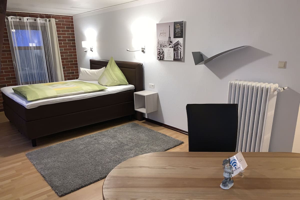 Ein modernes Schlafzimmer mit einem Bett, einem kleinen Tisch, einer Heizung und einem an der Wand montierten Regal.