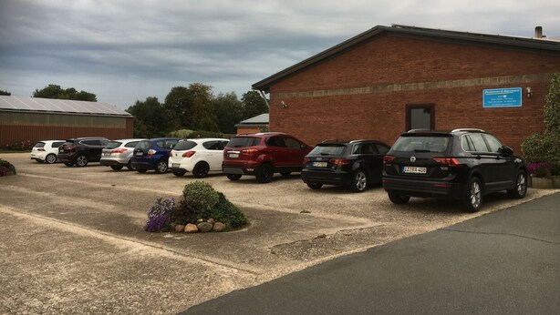 A parking lot with several cars parked in front of a building with a blue sign. - Apartment Sonnenaufgang near Airport (Elskop)
